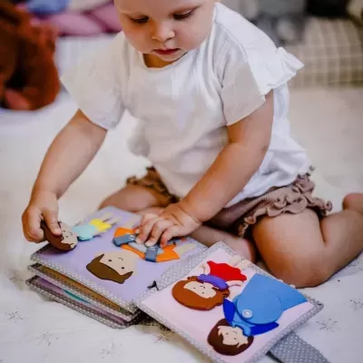 Criança a brincar com livro de tecido colorido e figuras destacáveis.