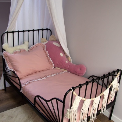 Cama de metal preto com roupa de cama rosa e peluche rosa, guirlanda de fios creme e cortinas brancas