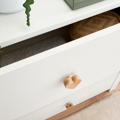 Gaveta branca com puxador de madeira em forma de nuvem aberta contendo tapete cinza e caixa de vime