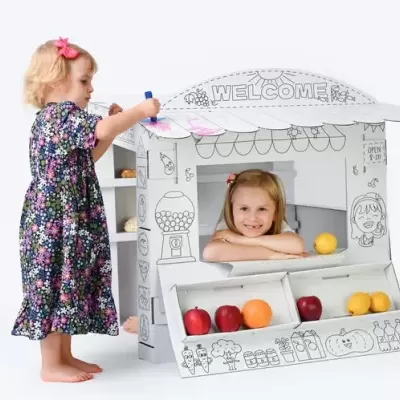 Duas crianças a brincar com casinha de cartão decorada para colorir com frutas artificiais