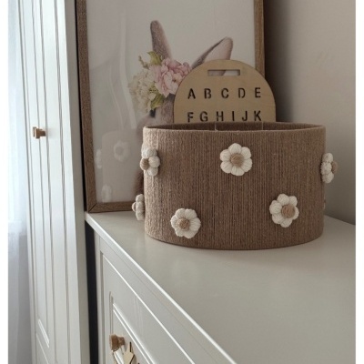 Cesto decorativo castanho com flores brancas sobre móvel branco com moldura de madeira e placa com letras