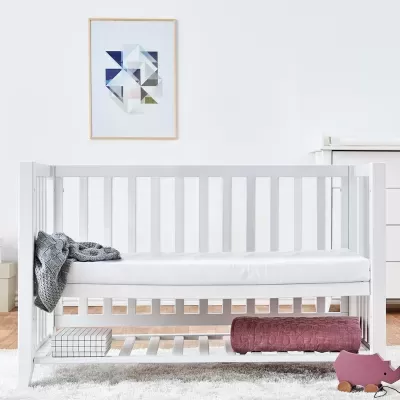 Berço branco de bebé com acessórios e quadro geométrico na parede