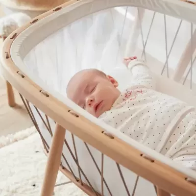 Mini berço de madeira clara com bebé a dormir no interior