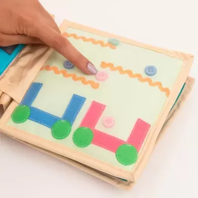 Livro infantil macio colorido com peças de velcro e botões, mão de criança interagindo