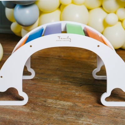 Arco de madeira colorido com suporte branco e balões ao fundo