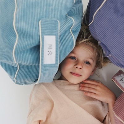 Criança de cabelos loiros deitada com almofadas azuis de veludo cotelê