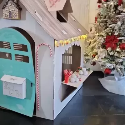 Casa de brincar infantil decorada para Natal ao lado de árvore de Natal
