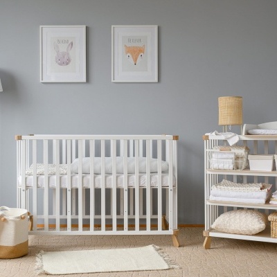 Quarto de bebé com berço branco, candeeiro de pé, prateleira com cestos e mantas, e duas molduras de animais na parede