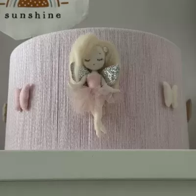 Cesto rosa decorativo com anjo e asas prateadas sobre móvel branco, cartaz ao fundo