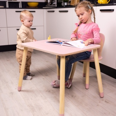 Mesa e cadeira infantis em madeira clara e rosa com crianças sentadas e em pé, em cozinha moderna.