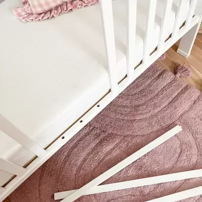 Berço branco com colchão branco e roupa de cama rosa xadrez sobre tapete rosa ondulado