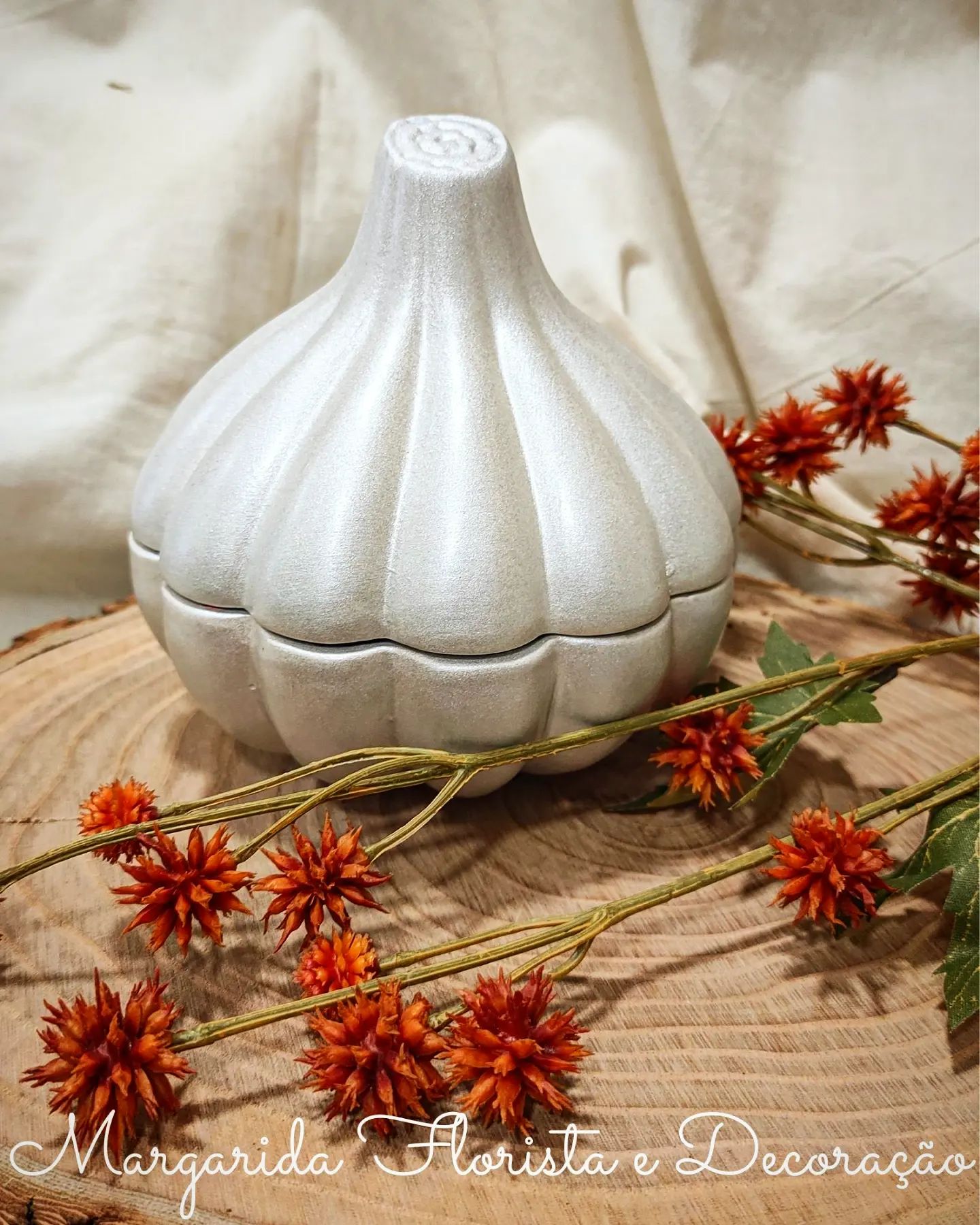 Frasco prateado em forma de alho com flores secas laranja sobre tábua de madeira