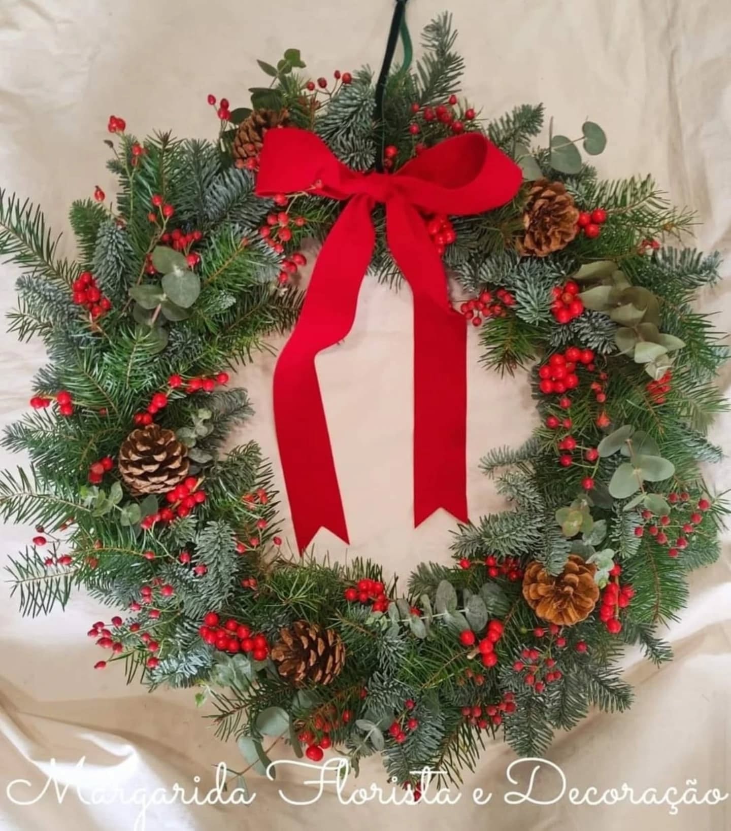 Guirlanda de Natal com ramos de pinheiro, bagas vermelhas, pinhas e laço vermelho