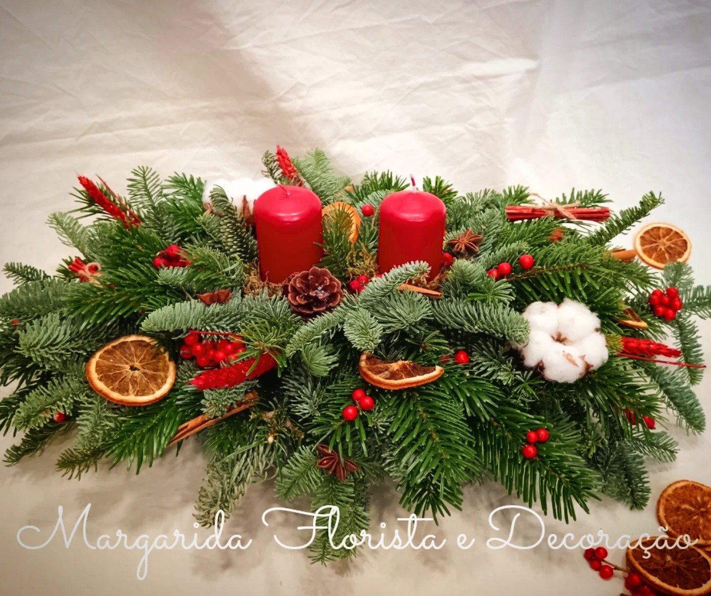 Centro de mesa natalício com velas vermelhas, ramos de pinheiro e decoração natural.