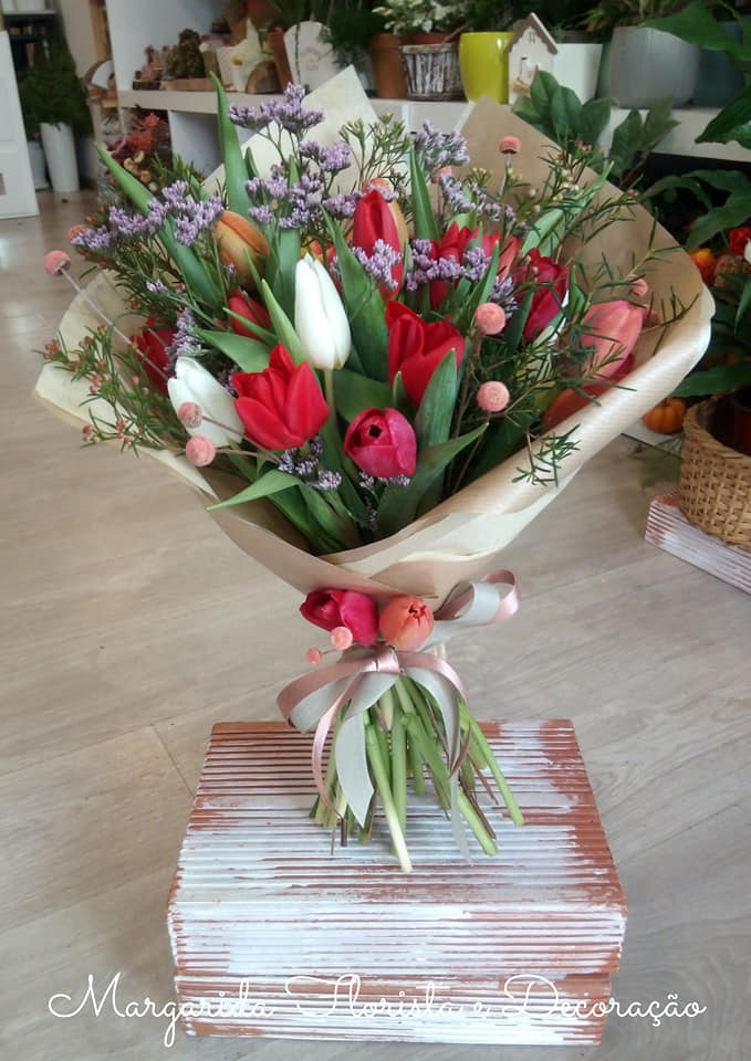 Bouquet de tulipas vermelhas e brancas com flores pequenas lilás e cor-de-rosa em papel castanho claro com fita rosa