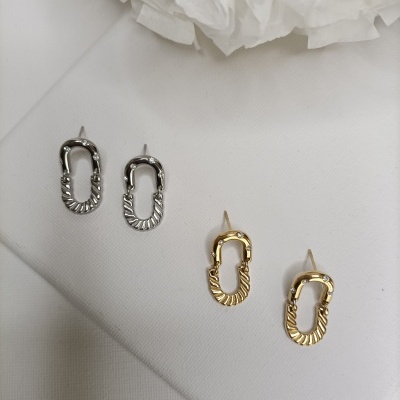 Brincos ovais prateados e dourados com textura e cristais sobre tecido branco