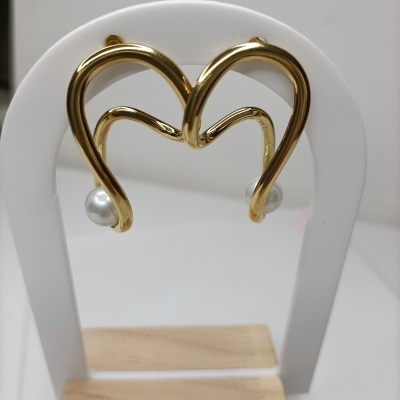 Brincos dourados em forma de coração com pérola, expostos num suporte branco com base de madeira.