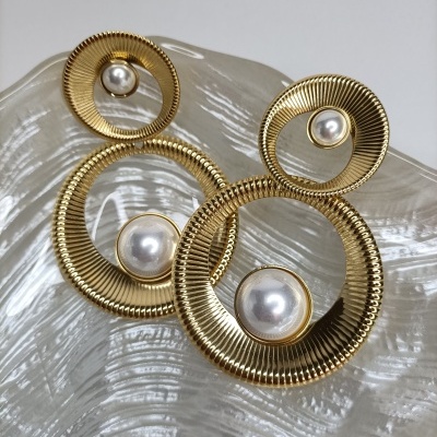 Brincos dourados redondos com pérolas sobre prato de vidro texturizado