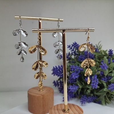 Brincos dourados e prateados em suportes de madeira com planta roxa ao fundo
