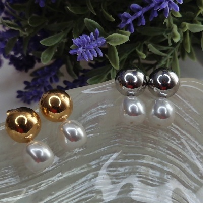 Brincos com bolas douradas e prateadas e pérolas pendentes sobre vidro texturizado com flores roxas