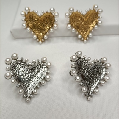 Quatro brincos em forma de coração, dois dourados e dois prateados, com pérolas ao redor, sobre fundo branco