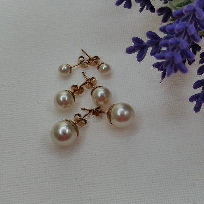 Brincos de pérola dourados de três tamanhos junto a flores roxas sobre fundo branco