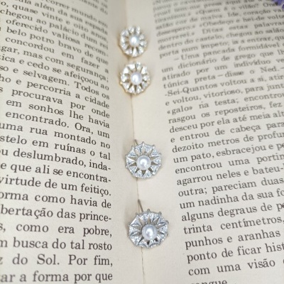 Quatro pares de brincos com pérola e pedras brilhantes sobre um livro aberto