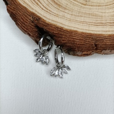 Brincos prateados com pendentes em forma de folhas sobre tecido branco e madeira