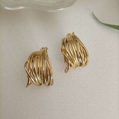 Brincos dourados entrelaçados sobre tecido branco com prato e folha verde