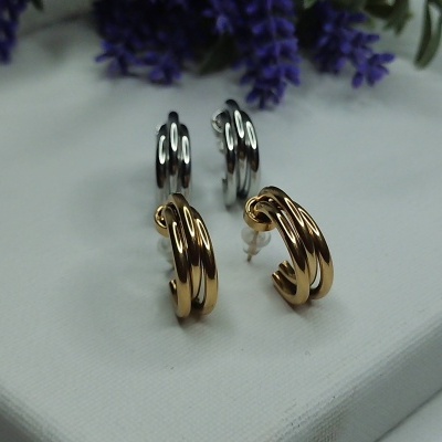 Brincos de argola dourados e prateados em superfície branca com flores roxas ao fundo