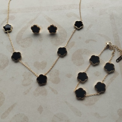 Conjunto de colar, brincos e pulseira dourados com pedras pretas em forma de flor sobre pano bege.