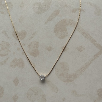 Colar dourado com pendente de pedra clara sobre superfície clara com padrões