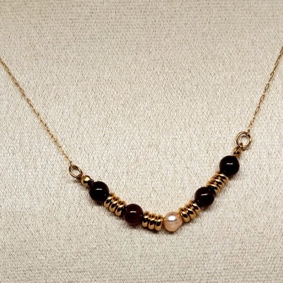 Colar dourado com contas pretas e contas peroladas num fundo bege.