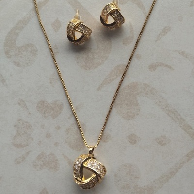 Conjunto de colar e brincos dourados com pedras brilhantes sobre fundo claro com padrões.