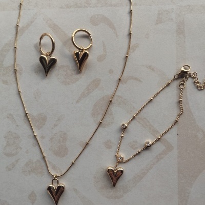 Conjunto de joalharia dourada com pendentes em forma de coração em fundo claro