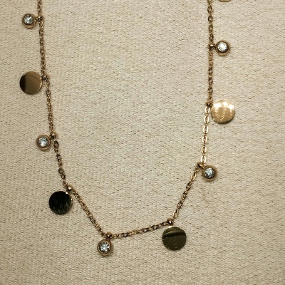 Colar dourado com pendentes redondos e pedras brilhantes sobre tecido bege