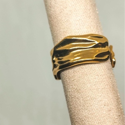 Anel dourado ondulado num suporte de tecido bege