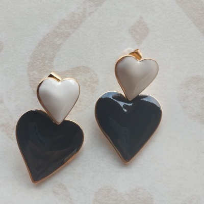 Brincos de coração branco e preto com contorno dourado sobre fundo claro