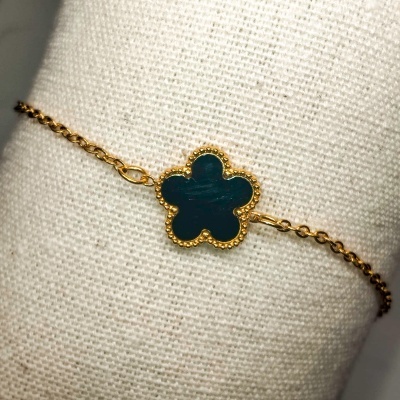 Pulseira dourada com pendente de flor verde sobre tecido claro