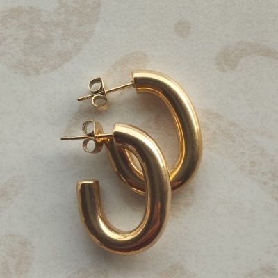 Brincos dourados em forma de elos curvos sobre superfície clara