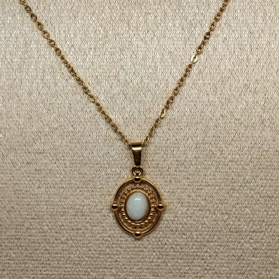 Colar com pendente oval dourado e pedra branca em fundo bege com textura