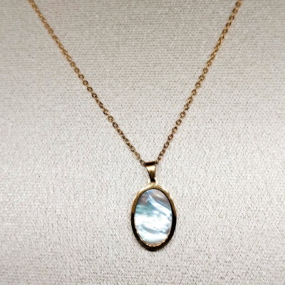 Colar dourado com pendente oval iridescente sobre tecido bege