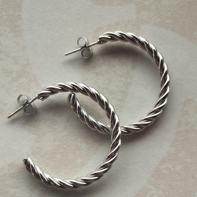 Brincos de argola prateados torcidos sobre fundo claro