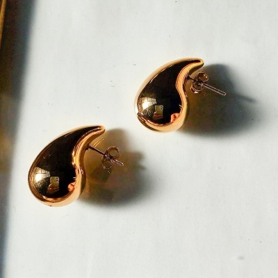 Brincos dourados em forma de gota sobre superfície branca