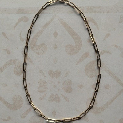 Colar de elos longos dourados sobre superfície decorativa.