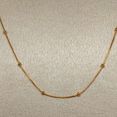 Colar dourado com esferas pequenas em fundo claro