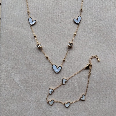 Colar e pulseira dourados com corações brancos sobre fundo cinza claro