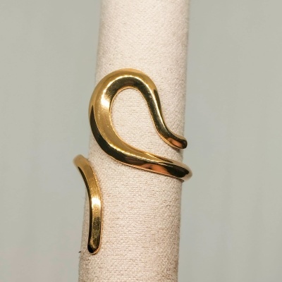 Anel aberto dourado com design curvilíneo em suporte de tecido bege