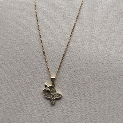 Colar dourado com pendente em forma de flor com brilhantes sobre fundo cinzento