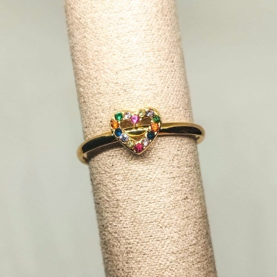 Anel dourado com coração colorido num suporte de tecido bege